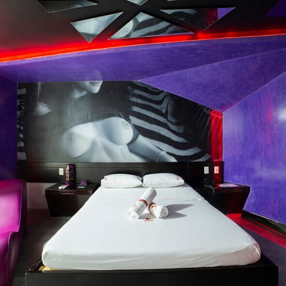 Arte monocromo viste una habitación de motel moderna, con iluminación vibrante roja y morada, complementada con muebles contemporáneos.