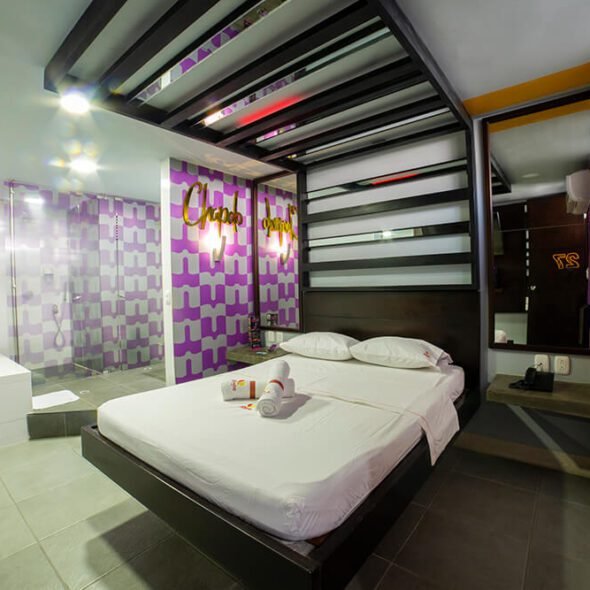 Moderno dormitorio en un motel de Bucaramanga, con pared morada de acento geométrico, baño integrado y muebles contemporáneos. Incluye jacuzzi.