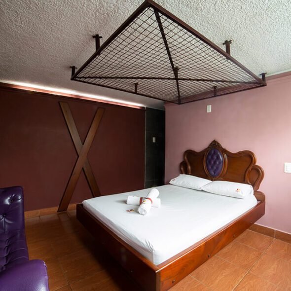 Moderno cuarto de motel con temática morada, resalta una cabecera en forma de X y una exclusiva decoración superior en rojo.