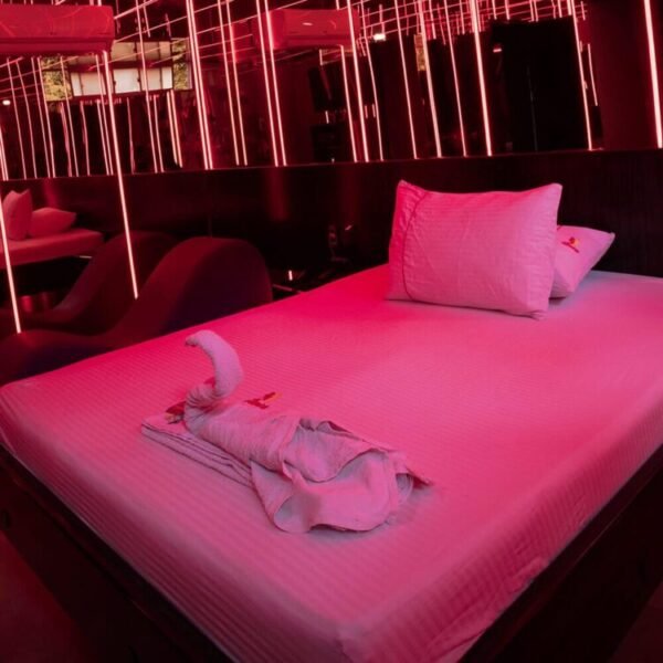 Un lecho perfectamente arreglado en un motel con jacuzzi, adornado con una toalla esculpida en forma de cisne, bajo seductora iluminación roja.