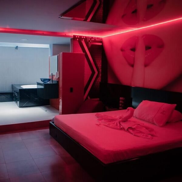 Estancia moderna con esquema rojo y negro, iluminada por neones rojos y decorada con arte gráfico sobre la cama; un motel que cuenta con jacuzzi.