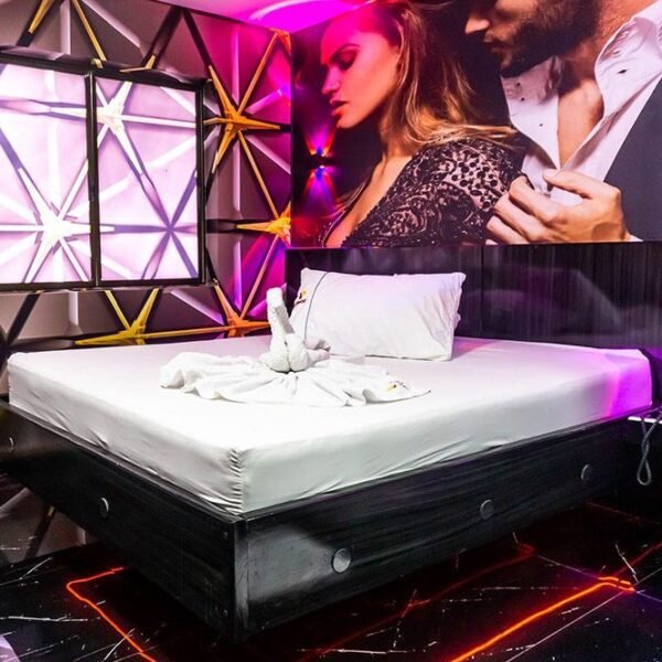 Una habitación de motel bañada en luces de neón, realza un mural urbano que muestra a una pareja en pleno baile.