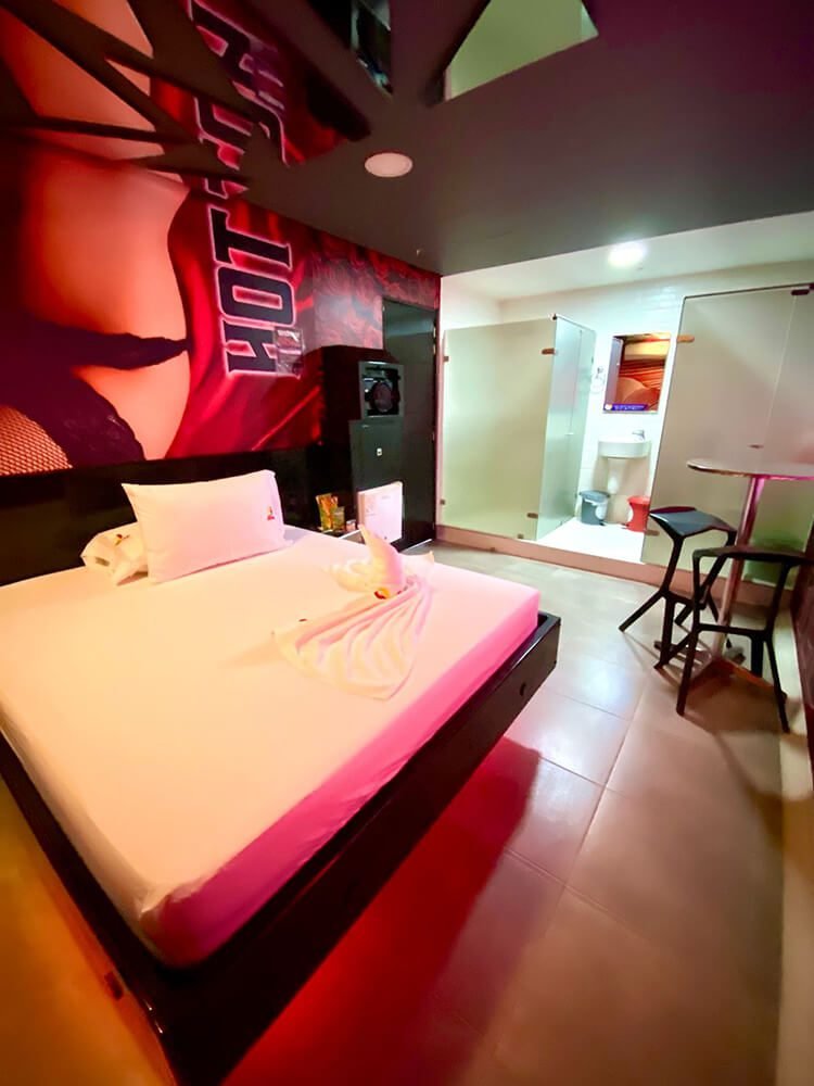 Habitación de hotel moderna y vibrante, con cama perfectamente hecha y toalla decorativa. Un rincón para sentarse y el baño sobresalen