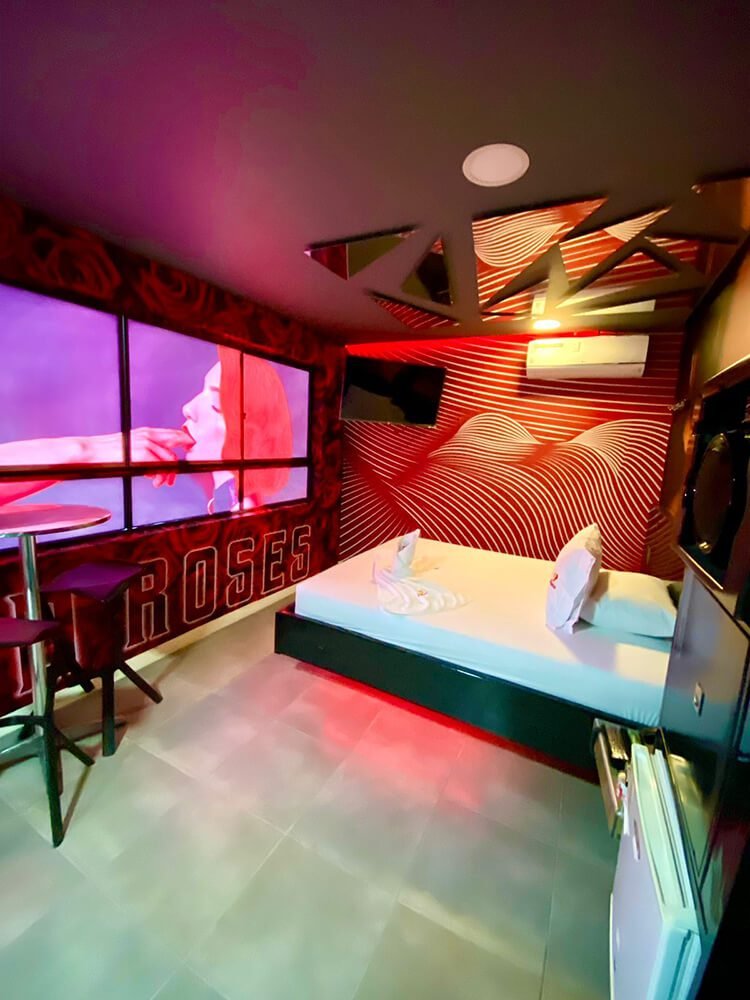 Un karaoke vibrante iluminado en rojo, con paredes geométricas y pantalla mostrando un cantante, ubicado en un motel con jacuzzi.