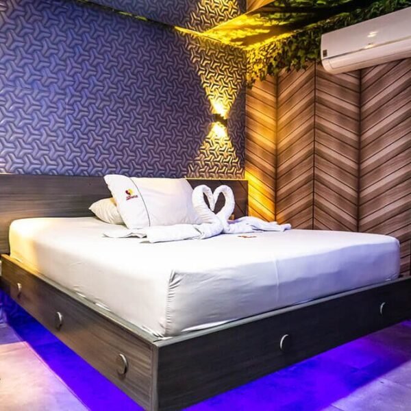 Las toallas de cisne adornan una cama impecable en una elegante habitación de motel de Bucaramanga, iluminada por luces caprichosas contra elegantes paredes.