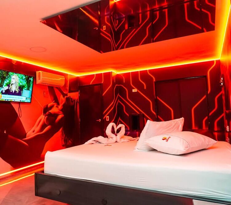 Habitación del motel iluminada por neón rojo, con una televisión incrustada en la pared.