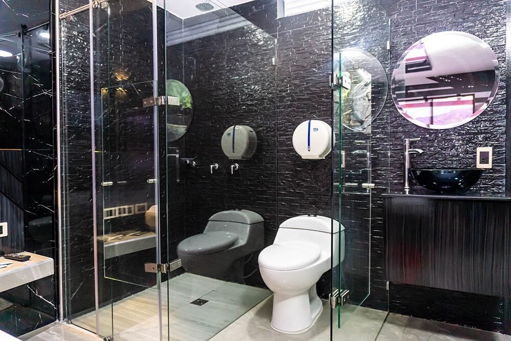 Un elegante baño de motel con paredes de azulejo negro, mampara de ducha de vidrio, instalaciones blancas y jacuzzi.