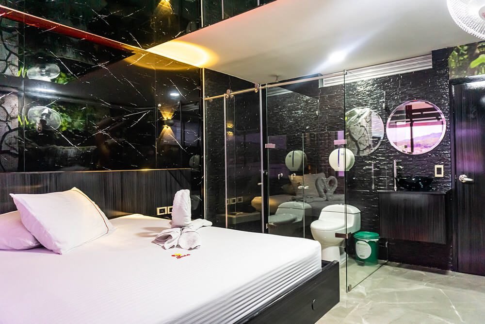 Contemporáneo dormitorio fusionado con baño vanguardista que exhibe paredes de cristal, azulejos de mármol negro y un lujoso jacuzzi.