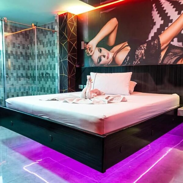 Una habitación contemporánea en motel con jacuzzi, destacando una iluminación vibrante y un gran mural sobre la cama.