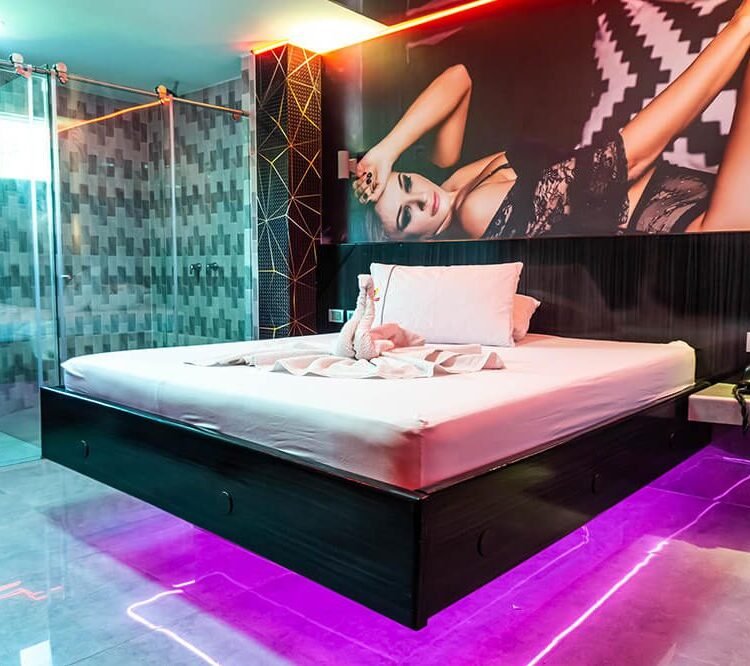 Una habitación contemporánea en motel con jacuzzi, destacando una iluminación vibrante y un gran mural sobre la cama.