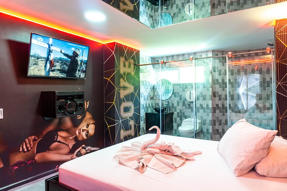 Cómoda y moderna habitación de motel con iluminación vibrante, amplia cama king y TV en la pared. Incluye un baño privado tipo suite y jacuzzi.
