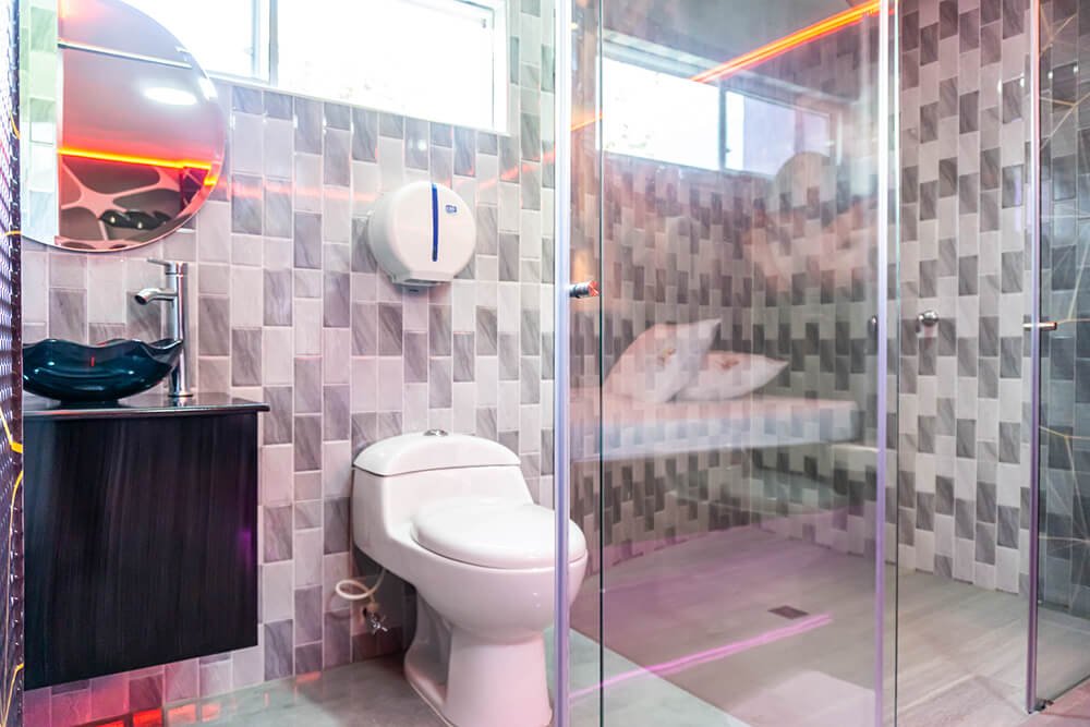 Un elegante baño de motel luce azulejos geométricos y una ducha de vidrio. El lavabo negro contrasta perfectamente.