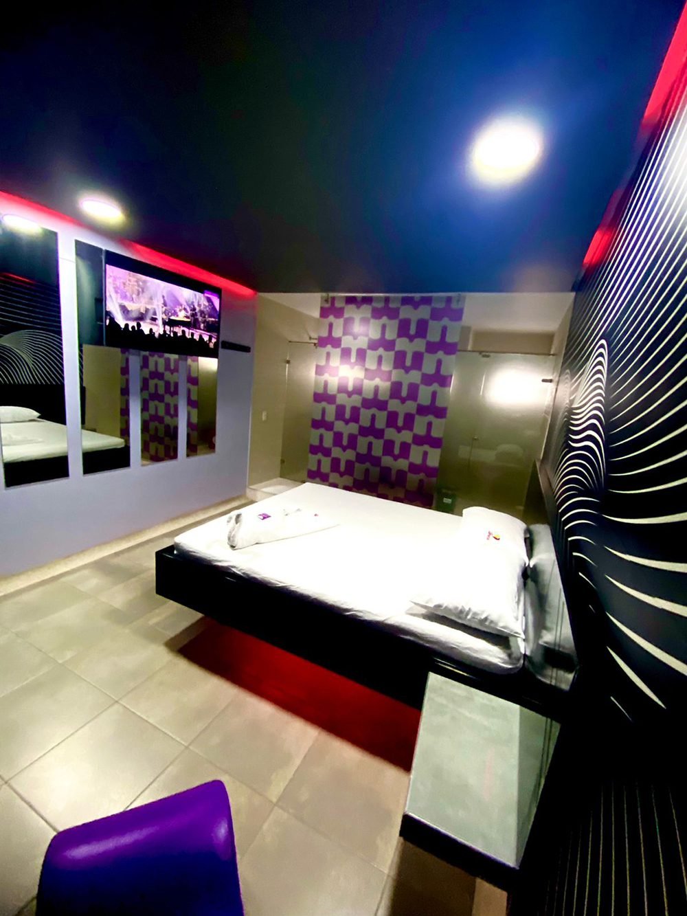 Un motel en Bucaramanga con un esquema de color púrpura y negro, destacando un jacuzzi y un televisor montado en la pared.