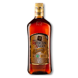 Una botella de añejo ron medellín, destacándose solitariamente contra un limpio fondo blanco en una habitación de motel.